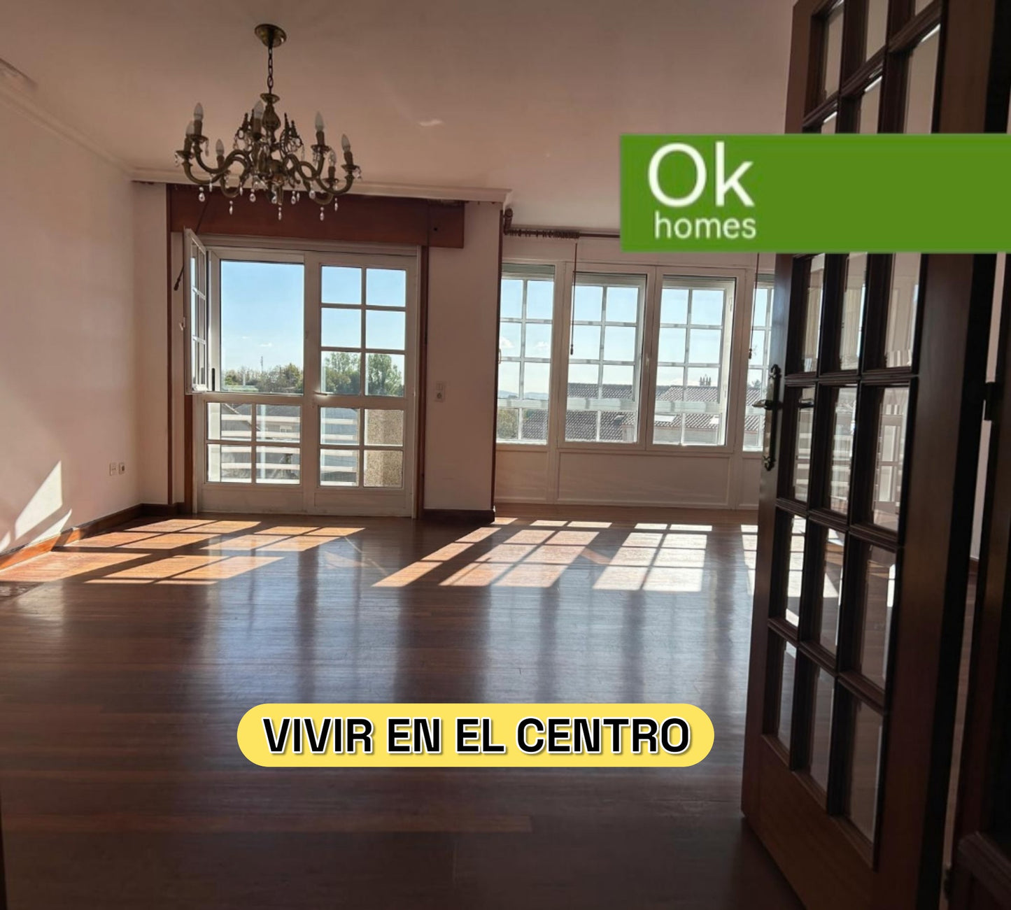 Salón luminoso y espacioso con suelos de madera y grandes ventanales en piso de OKHOMES en Melide