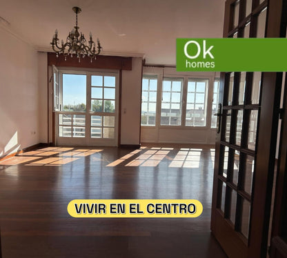 Salón luminoso y espacioso con suelos de madera y grandes ventanales en piso de OKHOMES en Melide